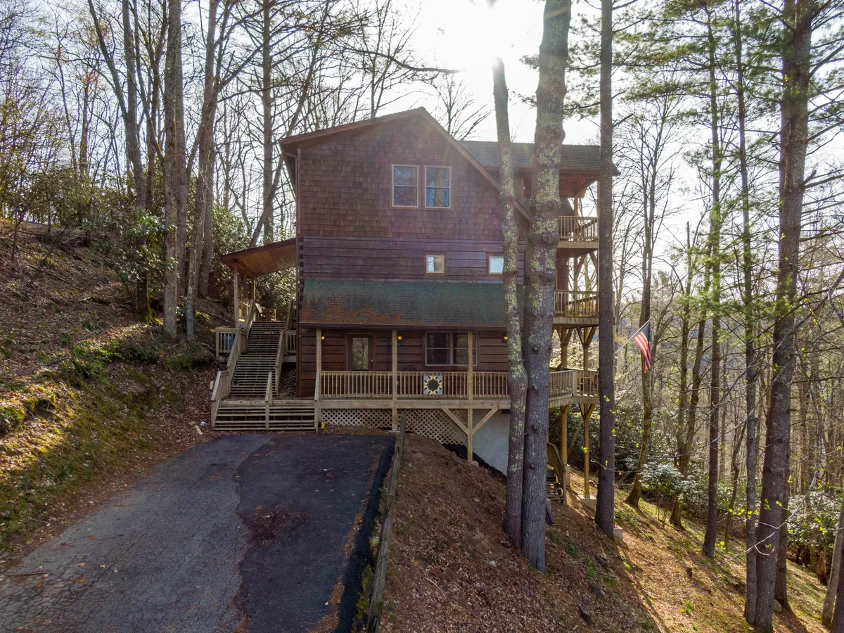 The exterior of the house showcases a spacious deck area surrounded by lush trees, with an American flag and inviting spaces for outdoor gatherings. The setting blends seamlessly into the nearby woods, suggesting easy access to nature trails and room for family barbecues or sunset watching.