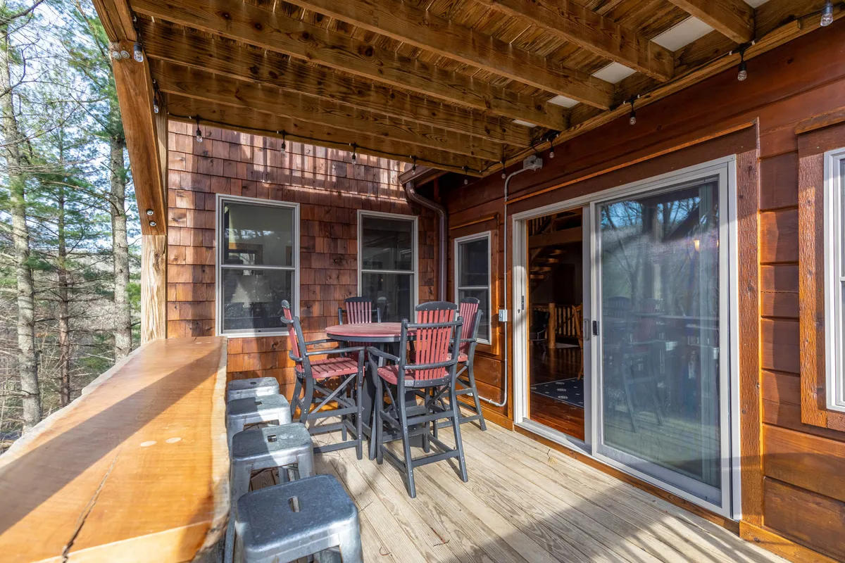 An inviting wooden deck with ample outdoor seating and sliding glass doors that connect the main living area to the outdoors. It depicts people enjoying outdoor dining, relaxing, and gathering with friends, surrounded by nature.