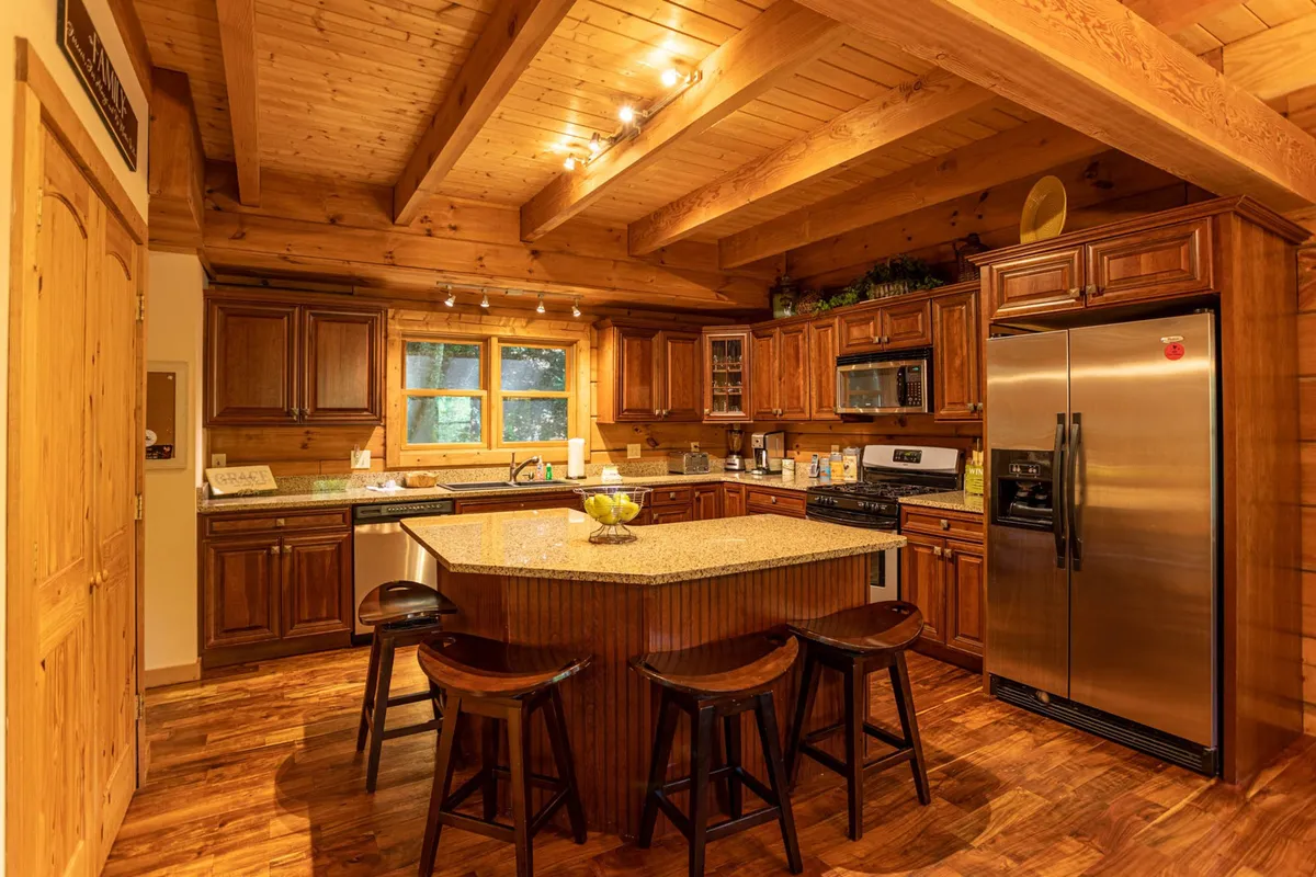 A chef-inspired kitchen with granite countertops, wooden cabinetry, a spacious island, stainless steel appliances, and a large window letting in natural light. The area is set for cooking, entertaining, and casual family gatherings.