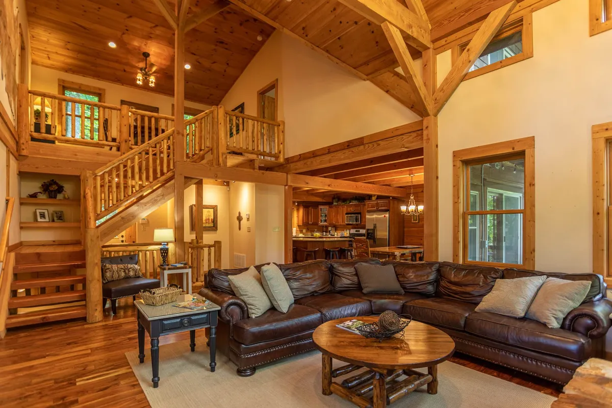 This image offers a sweeping view of the open-concept main level, featuring a large sectional sofa, wooden staircase, dining area, and a spacious kitchen with exposed wooden beams. The space radiates warmth and togetherness, highlighting areas where families can gather for meals, conversation, and relaxation.