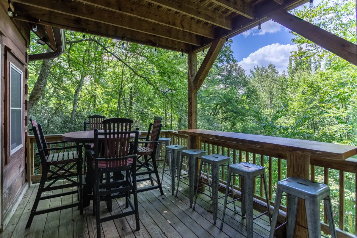 A tranquil exterior seating area is nestled among leafy greenery, featuring a sturdy wooden railing and comfortable seating. The serene forest backdrop and communal table highlight opportunities for socializing and enjoying nature.