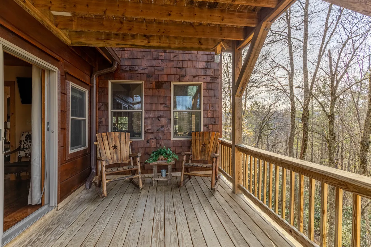 This image presents a peaceful wooden deck nestled among mature trees, featuring classic wooden rocking chairs positioned to enjoy the natural surroundings. The scene exudes tranquility, inviting guests to relax and soak in the serenity of the outdoors.